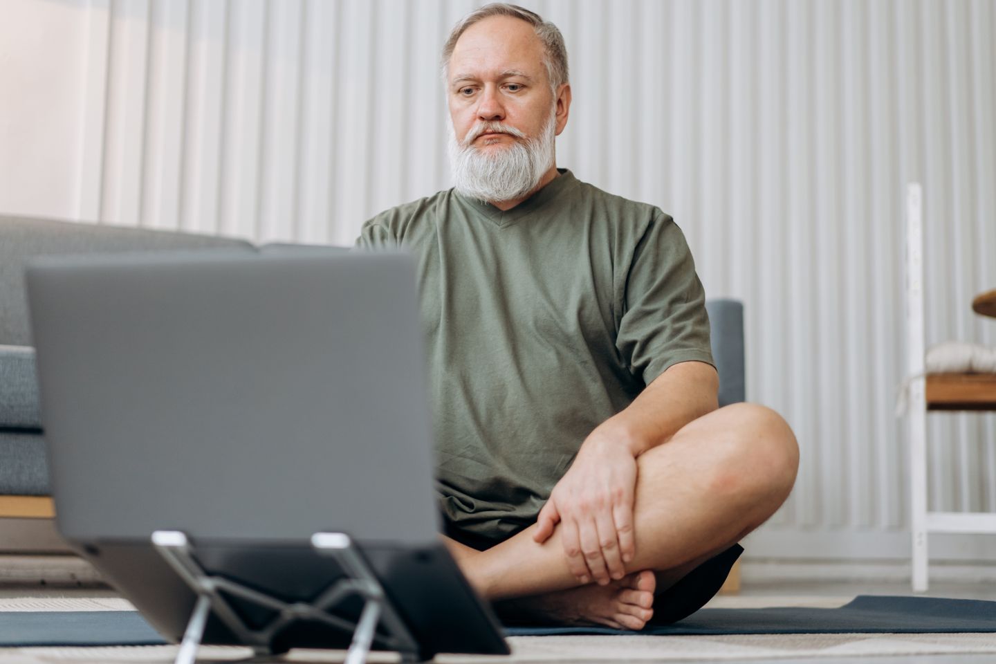 Senior man using a laptop for an online meditation session at home.