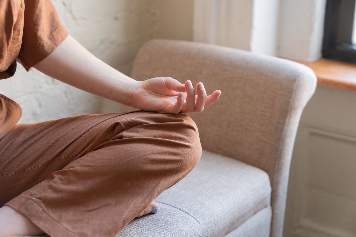 Close-up of a person meditating indoors on a comfortable armchair.